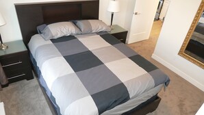Una cama bien hecha con colcha a cuadros, una lámpara de noche y una mesita de noche con cajones.