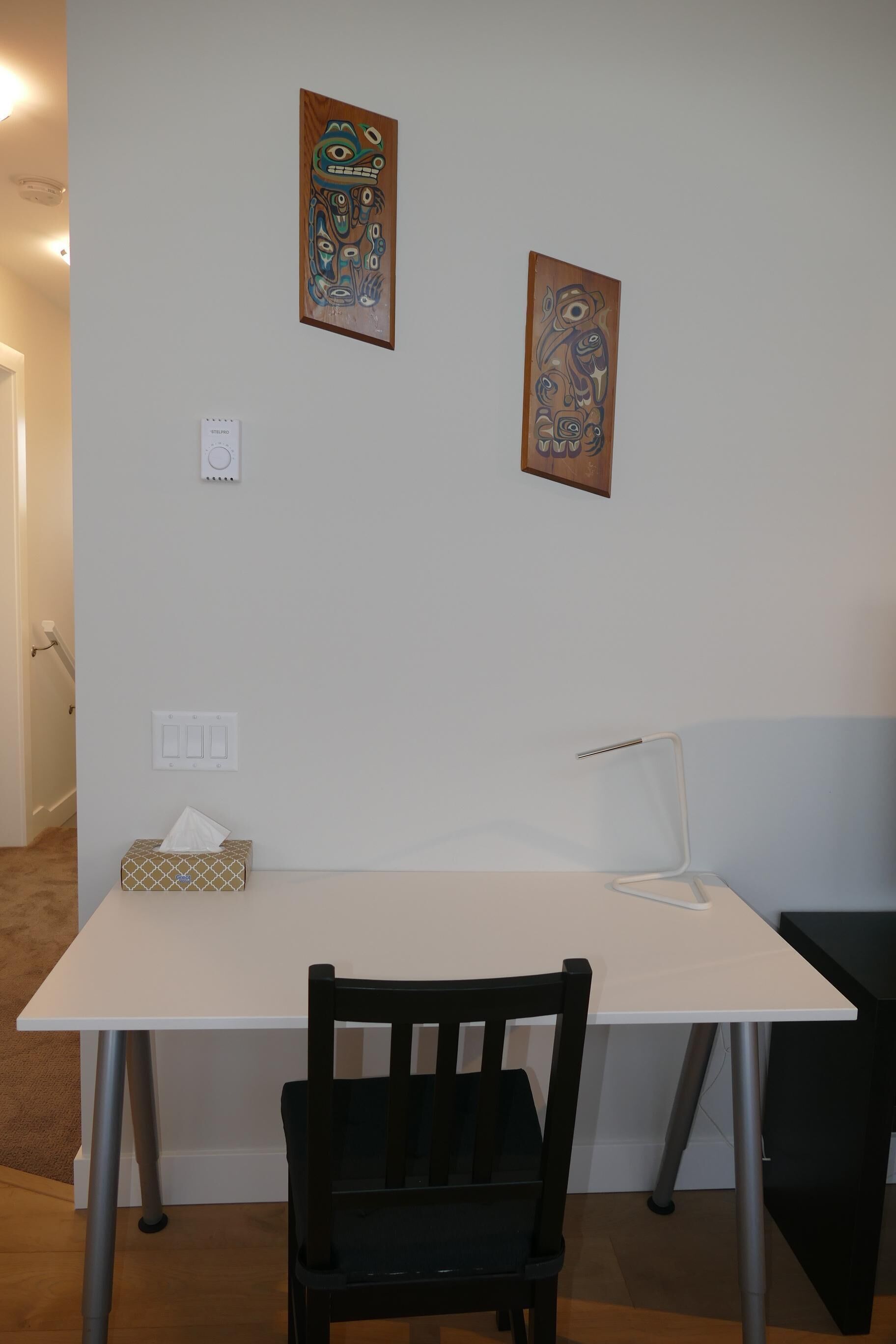 Une pièce avec un bureau blanc, une chaise noire et deux œuvres d’art encadrées accrochées au mur.