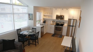 Cocina compacta con armarios blancos, refrigerador de acero inoxidable y comedor con mesa y sillas.