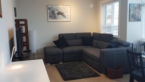 Una sala de estar moderna con un sofá modular, una mesa de comedor y un amplio ventanal con persianas.