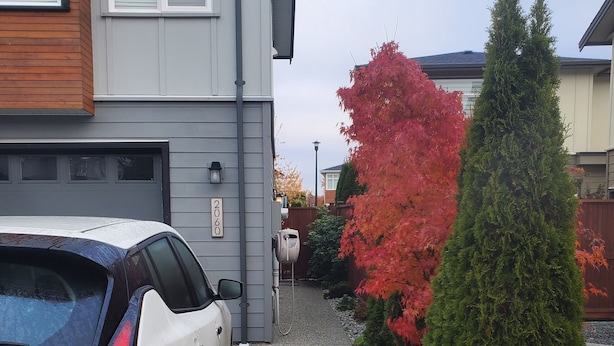 Una entrada de casa con un coche blanco estacionado a la izquierda, un buzón y una vivienda de color gris con el número '2060' en la pared.