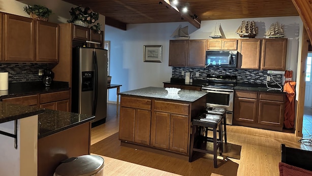 A modern kitchen with wooden cabinets, a stainless steel refrigerator, a microwave, and a large island with stools. - Bring your boats, jetskis, and LARGE family - so much space inside and out (Sylvan Beach)