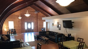 A spacious loft with a high ceiling, wooden walls, a black leather sofa, a dining table with chairs, and a flat-screen TV mounted on the wall. - Bring your boats, jetskis, and LARGE family - so much space inside and out (Sylvan Beach)