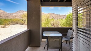 A balcony with a table and chair, overlooking a desert landscape with mountains and sparse vegetation.