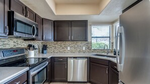 A modern kitchen with dark cabinets, stainless steel appliances, and a tiled backsplash.