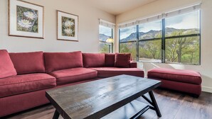 A living room with a red sectional sofa, a wooden coffee table, and a large window offering a mountain view.
