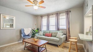 A living room with a ceiling fan, a light fixture, a sofa, a chair, a coffee table, a plant, and a small bar area.