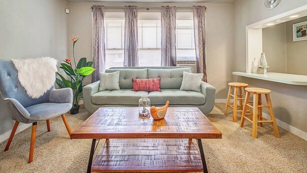 A living room with a sofa, a chair, a coffee table, and a bar area with stools.