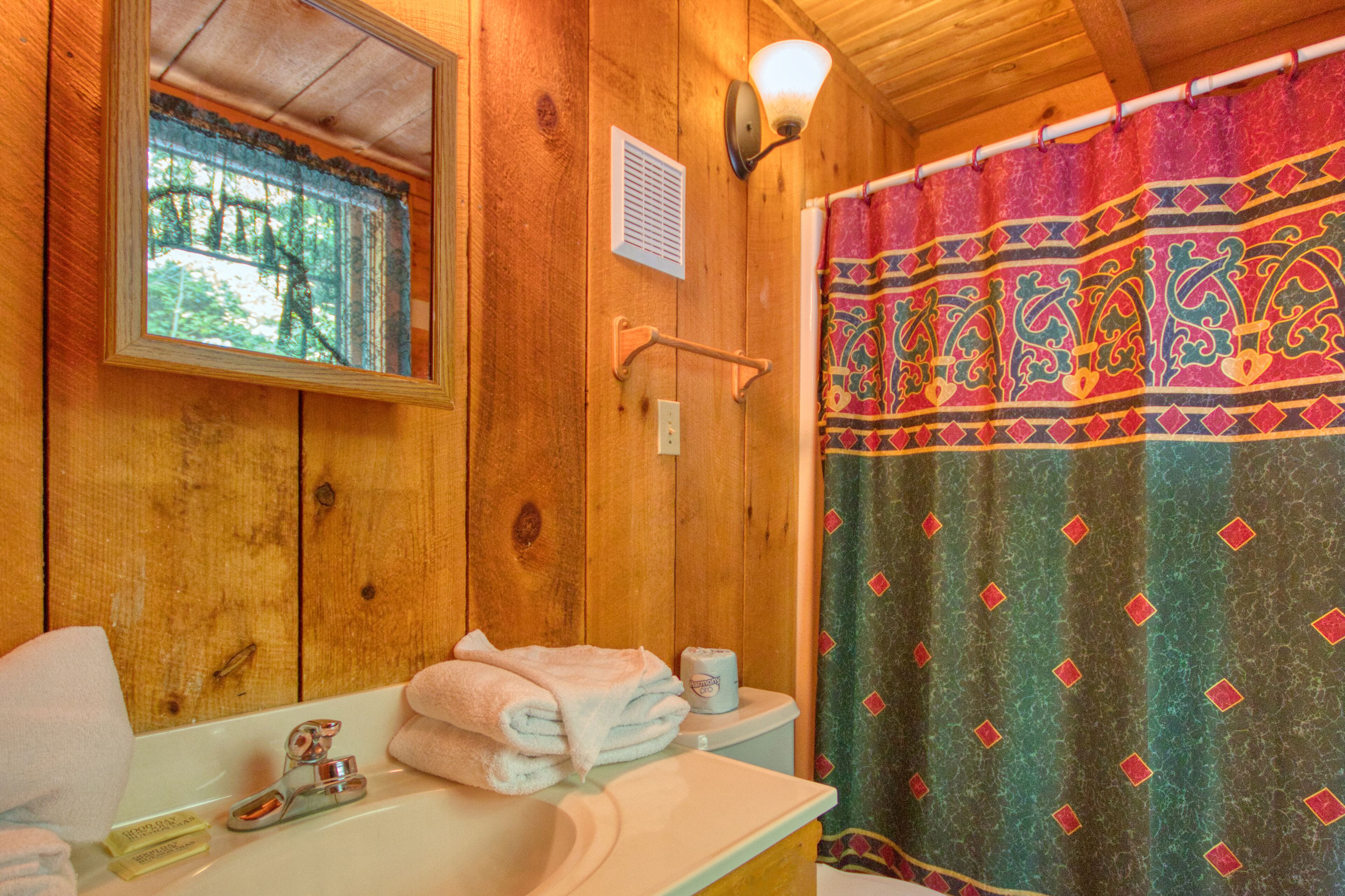 A wooden bathroom with a sink, mirror, and a shower curtain with a geometric pattern.