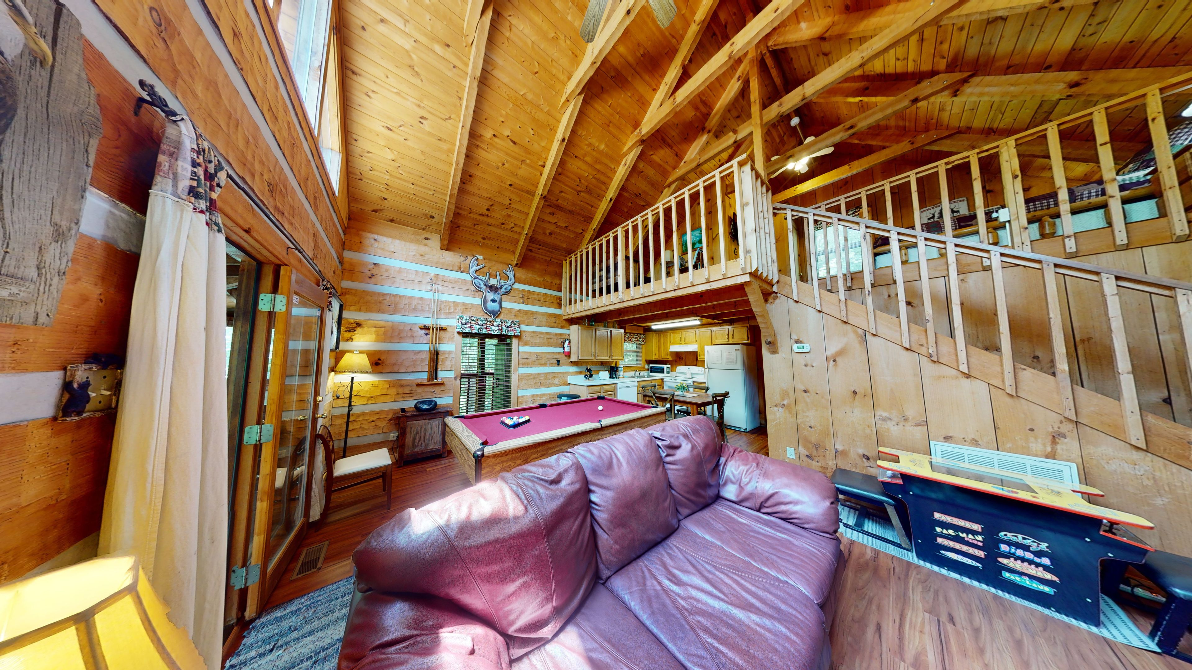 A cozy cabin interior with a pool table, a leather sofa, and a staircase leading to an upper level.