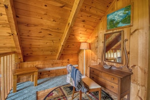 A wooden cabin interior with a wooden bench, a dresser with a mirror, and a painting on the wall.