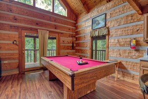 A wooden cabin with a pool table, a door leading to a balcony, and a fire extinguisher mounted on the wall.