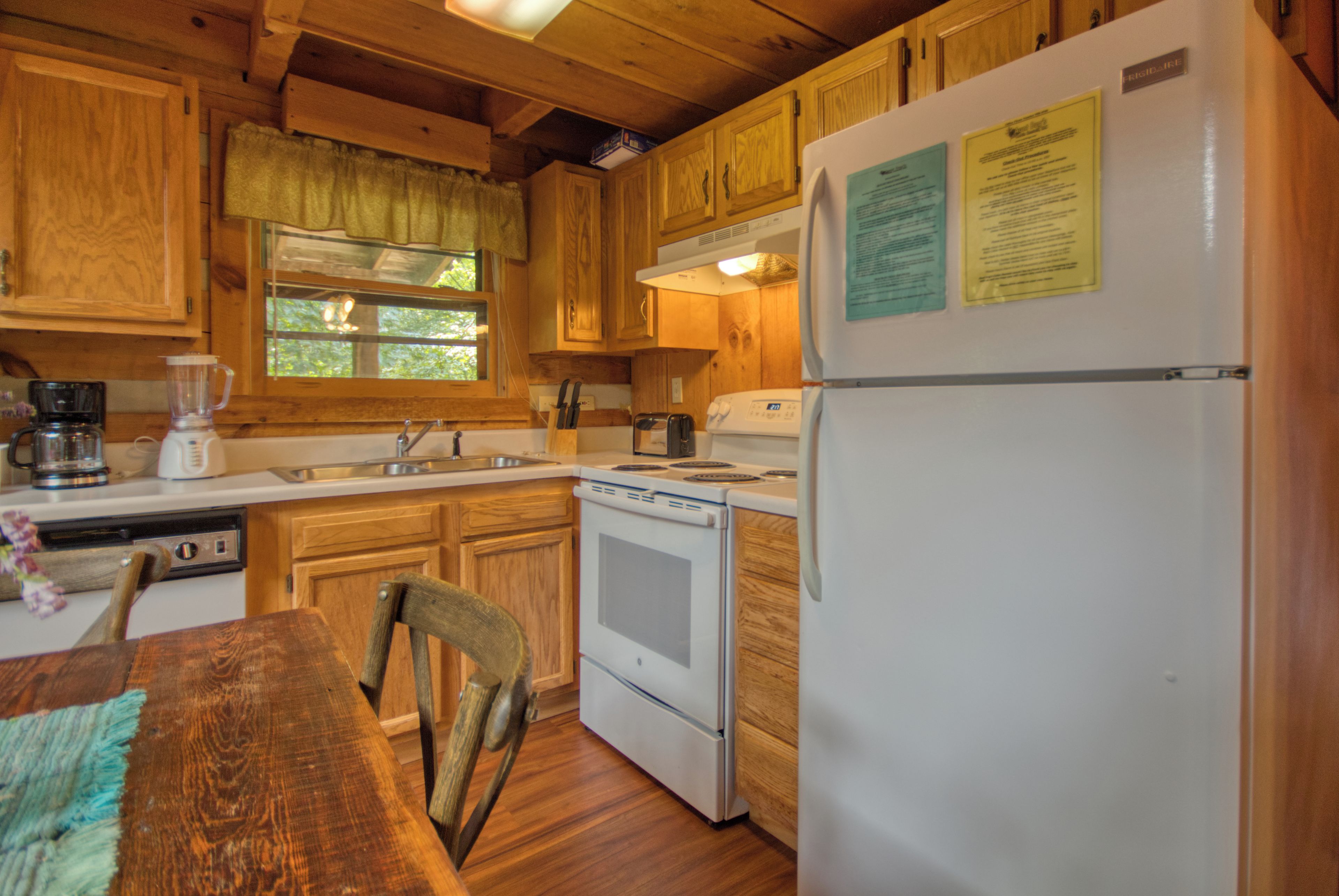 Une cuisine rustique, située dans une cabane en bois, équipée d’un réfrigérateur, d’une cuisinière, d’un évier et de meubles de rangement en bois.