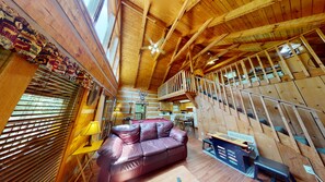 A wooden interior with a sofa, a pool table, and a staircase.