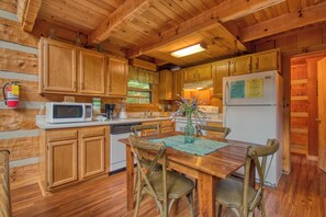 A wooden cabin kitchen with wooden cabinets, a microwave, a refrigerator, and a dining table with chairs.