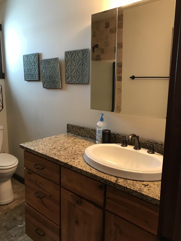 A bathroom with a granite countertop, a white sink, a mirror, and three textured wall art pieces. - Cozy cabin in a beautiful mountain valley close to hiking, golf, airport, skiing (Belgrade)