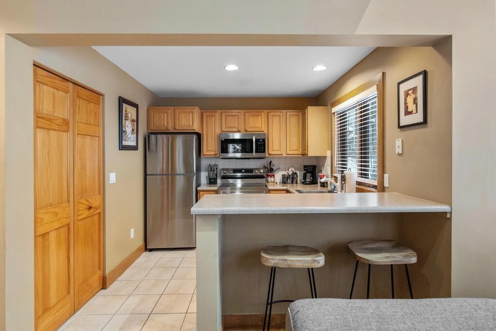 A compact kitchen with wooden cabinets, stainless steel appliances, and a central island with stools.