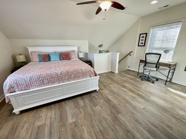 A bedroom with a bed, a desk, a chair, a ceiling fan, and a window with blinds.