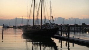 Un gran barco velero amarrado en un puerto deportivo, con agua tranquila que refleja el barco y el muelle.