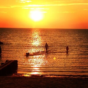 A sunset over a calm sea with three people standing in the water. - Cape Escape-Short Walk to Beach, Pet Friendly, Fenced Yard & Optional GC Rental (Cape Charles)