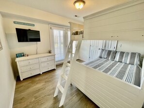 A bedroom with a bunk bed, a dresser, a television, and a window with blinds. - Cape Escape-Short Walk to Beach, Pet Friendly, Fenced Yard & Optional GC Rental (Cape Charles)
