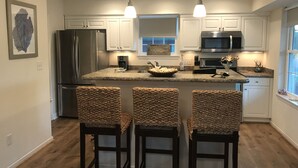 Una cocina moderna con armarios blancos, un refrigerador de acero inoxidable, un microondas y una isla grande con taburetes de bar.