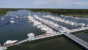 Una marina con numerosos barcos amarrados, un muelle largo y un pequeño edificio al final.
