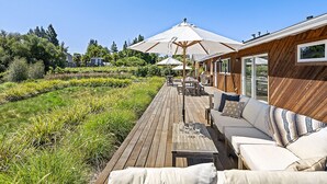 A wooden deck with outdoor seating, umbrellas, and a view of a house in the background.