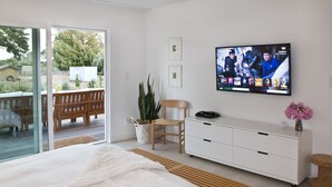 A bedroom with a large bed, a TV mounted on the wall, a wooden chair, a white dresser, and a sliding glass door leading to an outdoor area.