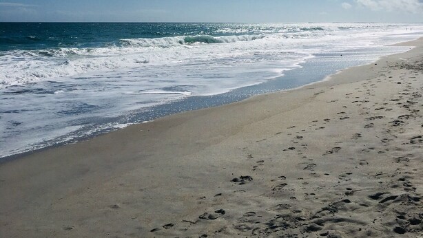 A beach with footprints in the sand and waves crashing onto the shore. - Prime location and the perfect getaway for two (Wrightsville Beach)