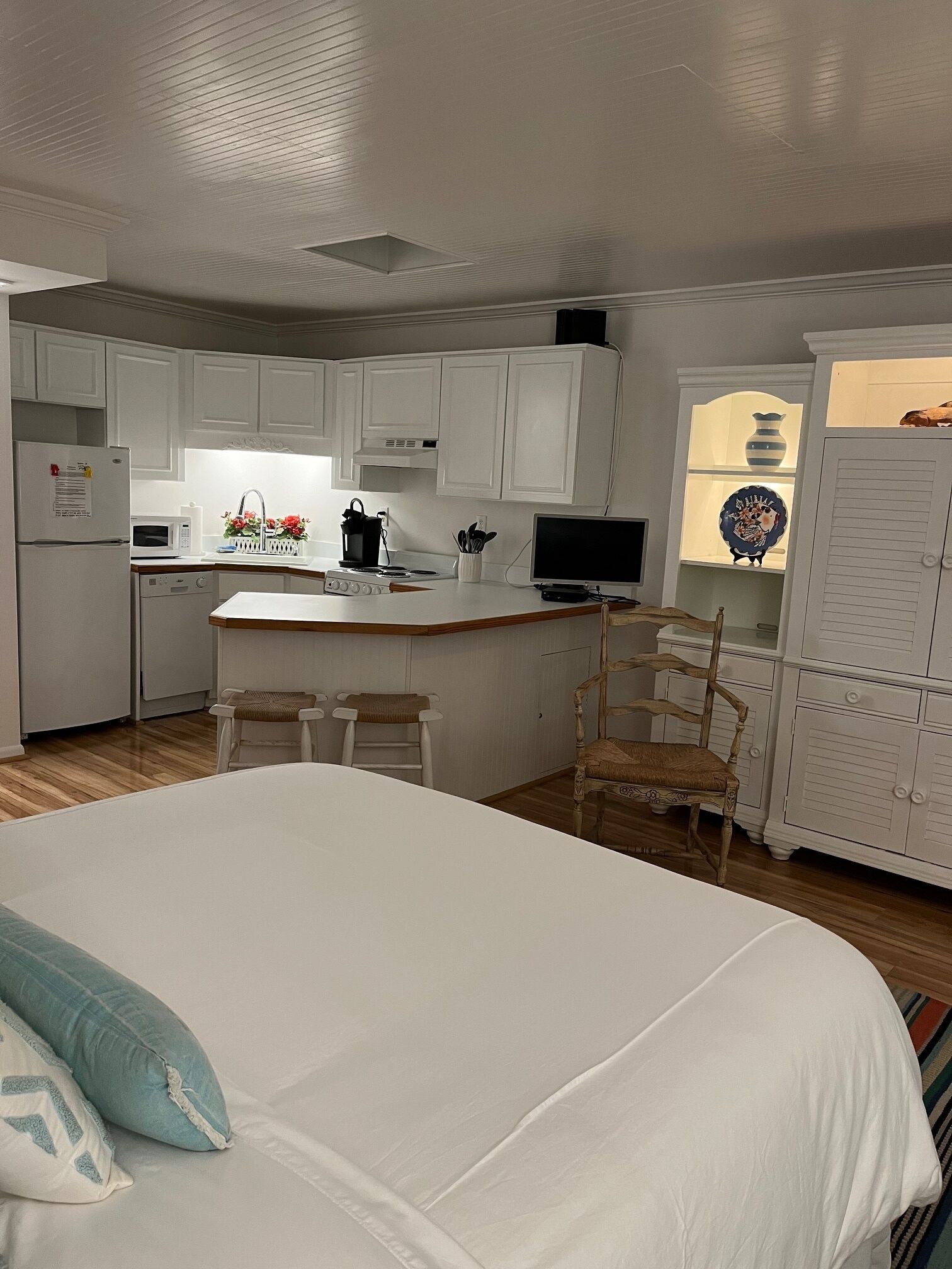Una cocina compacta y moderna con armarios blancos, una isla central con taburetes y un comedor con una silla de madera.
