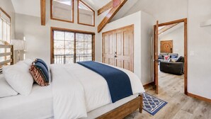 Een slaapkamer met een groot bed, houten balken in het plafond, een garderobe en uitzicht op de woonkamer.