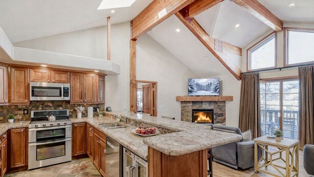 Een ruime keuken met granieten aanrechtbladen, houten kastjes en een stenen openhaard.