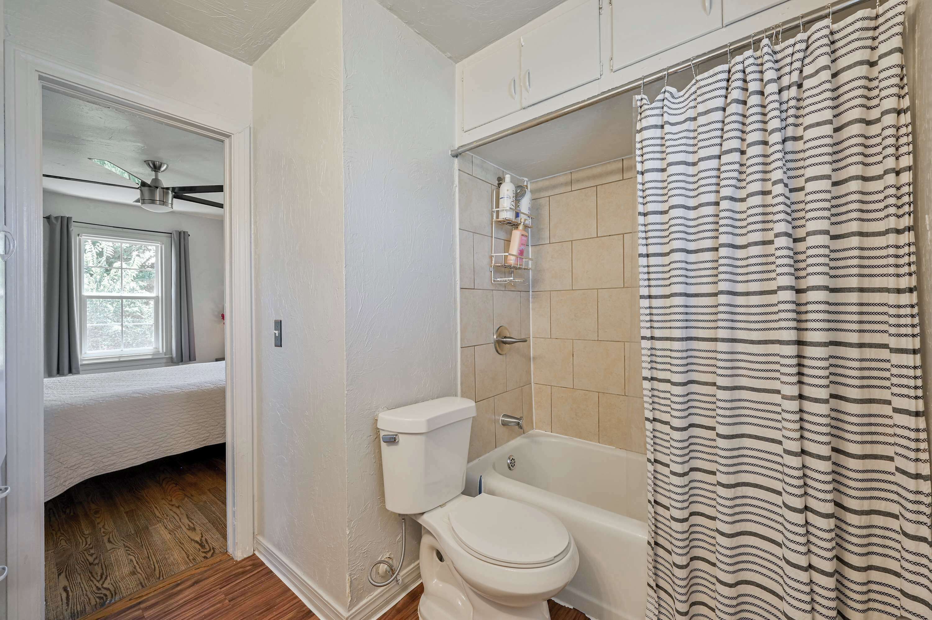 Une salle de bain équipée de toilettes, d’une baignoire, d’un rideau de douche et d’une fenêtre avec des rideaux.