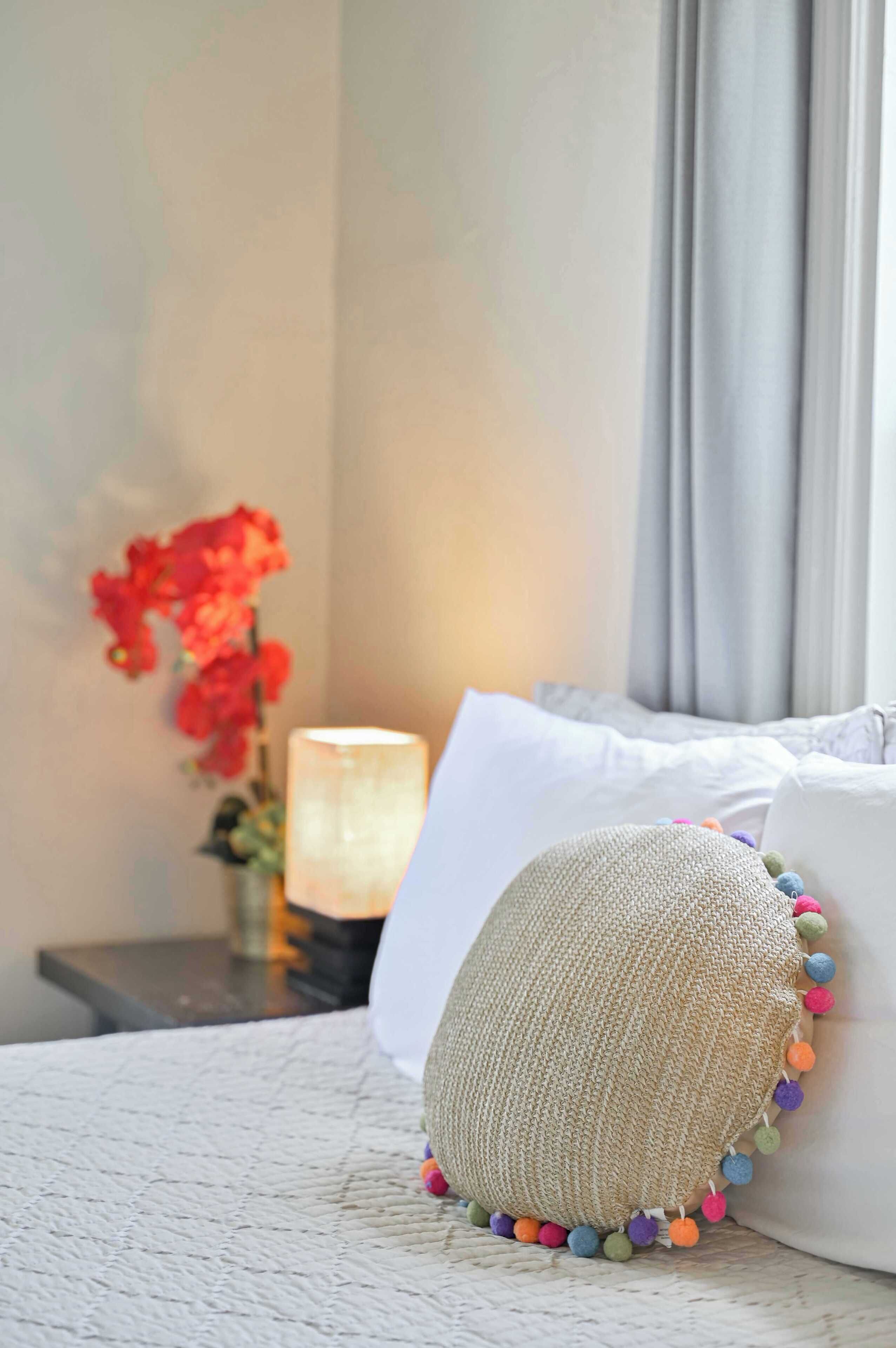 A bed with a white pillow and a textured pillow with colorful pom-poms.