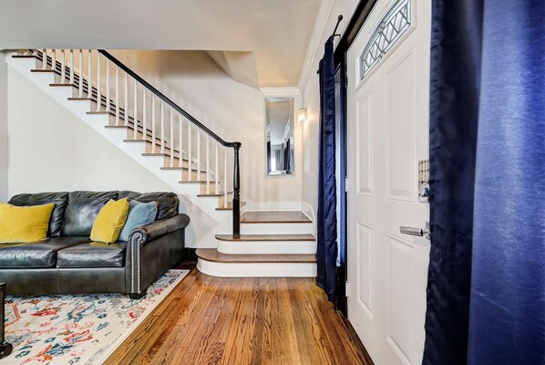 A staircase with white railings, a black leather sofa with yellow cushions, and a patterned rug.