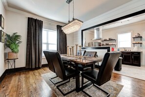 A dining area with a wooden table, black chairs, a chandelier, and a potted plant.