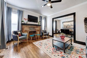 A living room with a fireplace, a television, a ceiling fan, and a dining area with chairs and a table.
