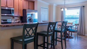 A modern kitchen with stainless steel appliances, wooden cabinets, and a breakfast bar with chairs. - Available 2025 !! Beautiful Water View 2 Bed+ Den +Garage Veranda Treviso Bay (Naples)