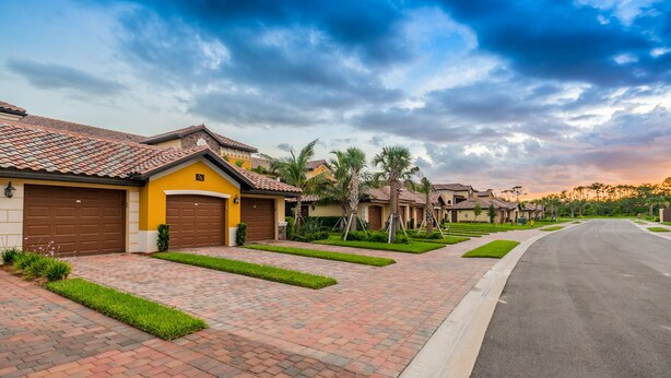 A residential street with houses featuring red-tiled roofs, brick driveways, and well-maintained lawns. - Available 2025 !! Beautiful Water View 2 Bed+ Den +Garage Veranda Treviso Bay (Naples)