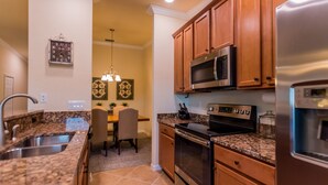 A kitchen with granite countertops, stainless steel appliances, wooden cabinets, and a dining area with a chandelier. - Available 2025 !! Beautiful Water View 2 Bed+ Den +Garage Veranda Treviso Bay (Naples)