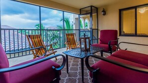 A balcony with red chairs, a table, and a view of palm trees and mountains. - Available 2025 !! Beautiful Water View 2 Bed+ Den +Garage Veranda Treviso Bay (Naples)