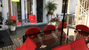 An outdoor patio with red chairs and a glass table, surrounded by potted plants and a yellow umbrella. - LA VIE EST BELLE - 4+1BEDroom -  Free Parking - A/C  (Montréal)