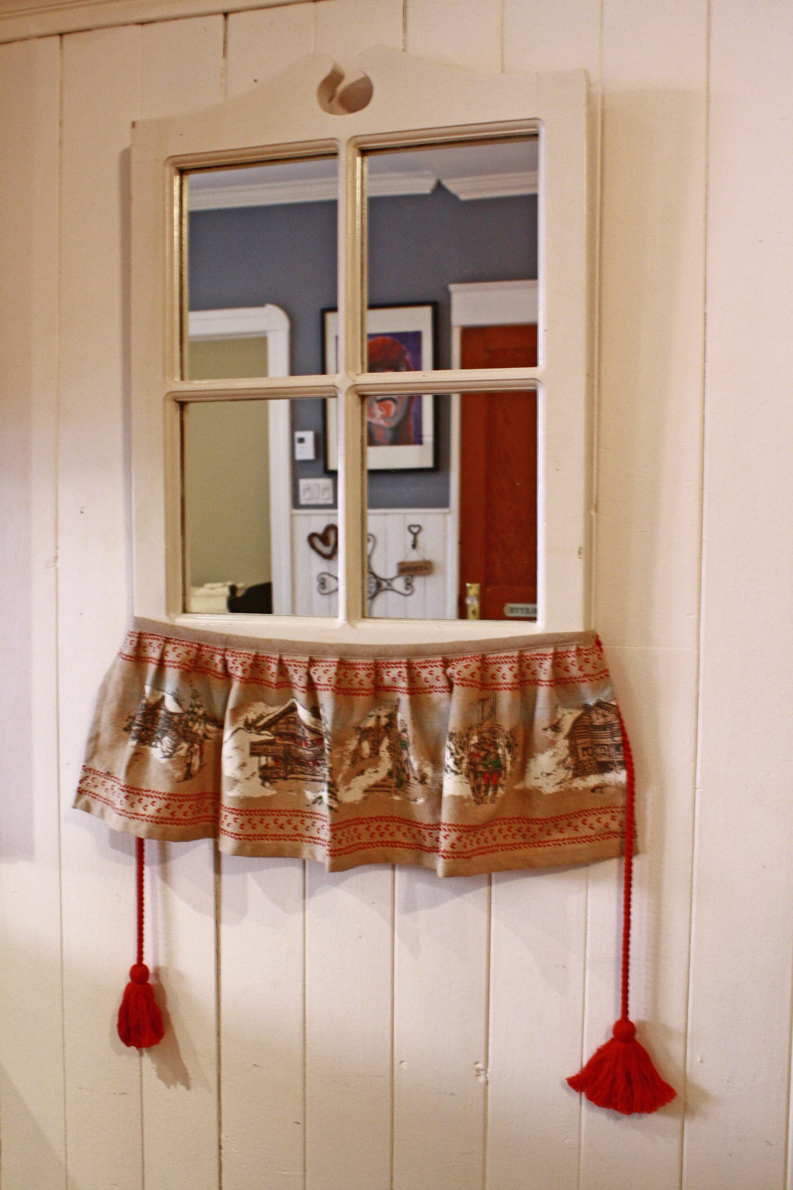 Una ventana con cortina decorativa que muestra una escena campestre y flecos.
