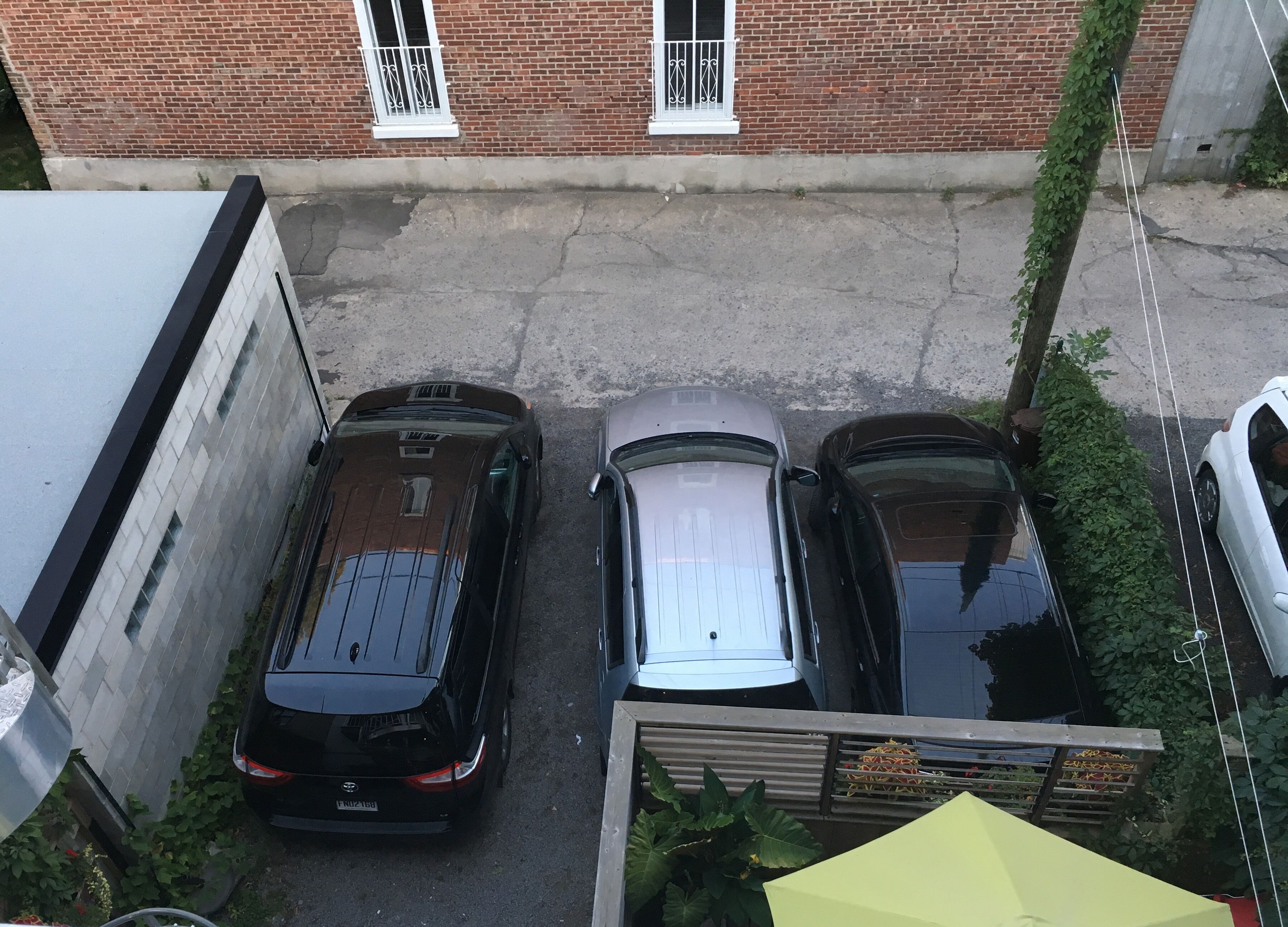 Eine schmale Straße mit drei parkenden Autos und einem Gebäude mit Backsteinfassaden und weißen Fensterrahmen.
