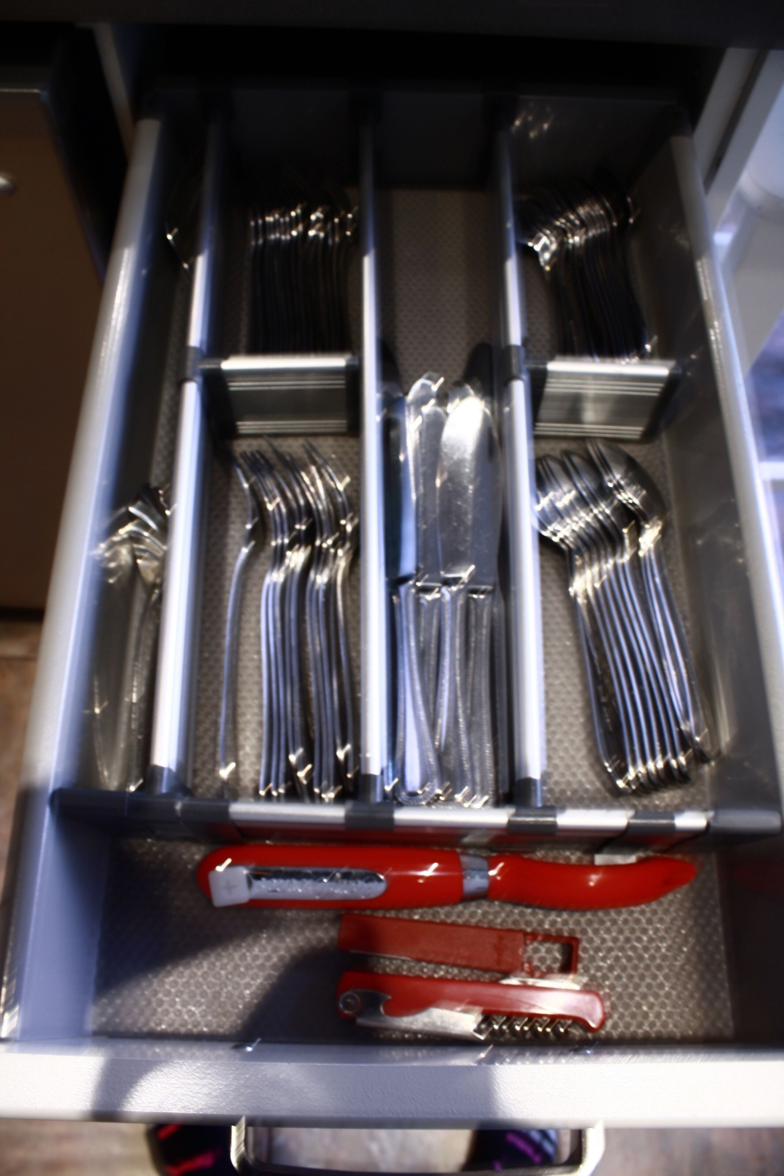 A drawer with utensils and a red tool.