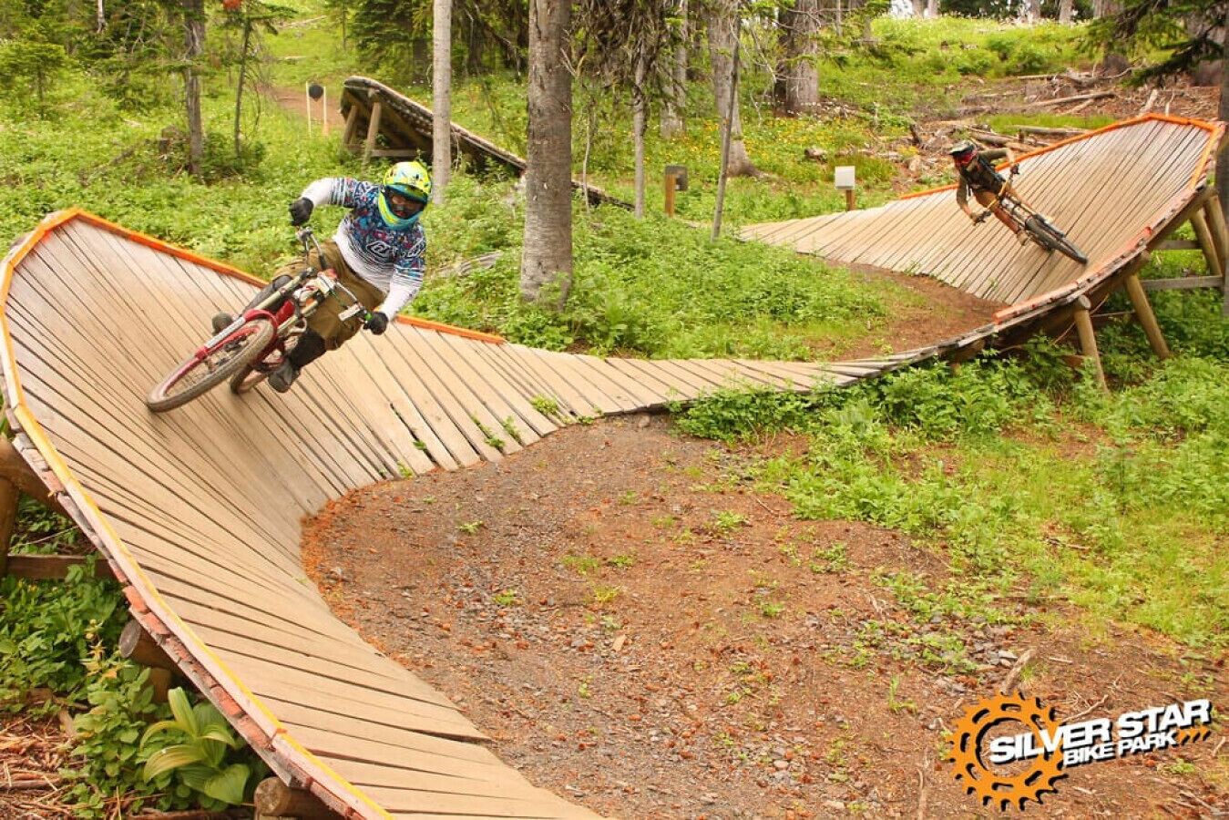 Un parcours de VTT avec des rampes en bois et un sentier de terre, le tout entouré de verdure.