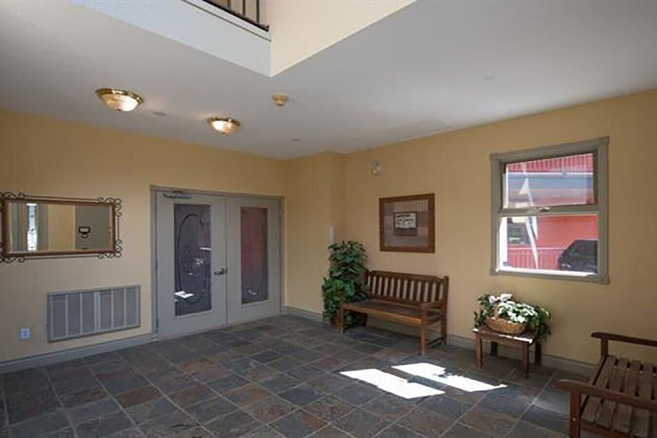 Un hall d’entrée spacieux, doté d’un sol carrelé, d’un banc, d’une plante en pot et d’un tableau encadré accroché au mur.