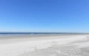 A wide sandy beach with a clear blue sky.