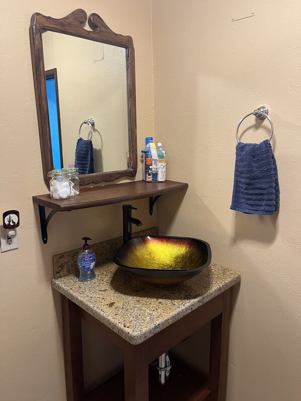 A bathroom with a vanity, a sink with a bowl, a mirror, a towel rack, and a soap dispenser.